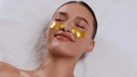 Woman relaxing with gold under-eye patches on a towel